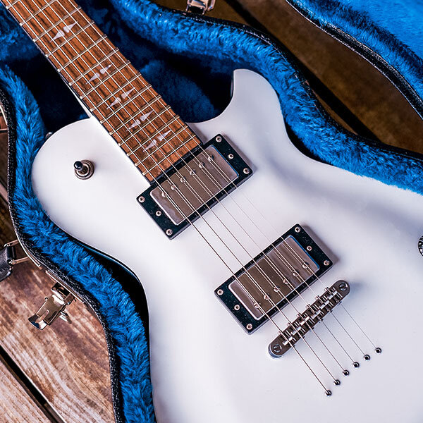 closeup of body of white electric guitar in hardshell case with blue interior