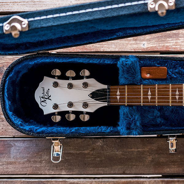closeup of headstock of white electric guitar in hardshell case with blue interior
